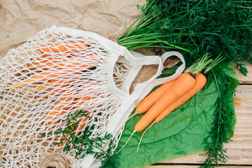 Eco-friendly mesh shopping bag with freshly picked carrots, on a wooden background.Zero waste,...