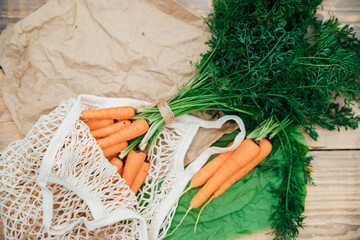 Eco-friendly mesh shopping bag with freshly picked carrots, on a wooden background.Zero waste,...