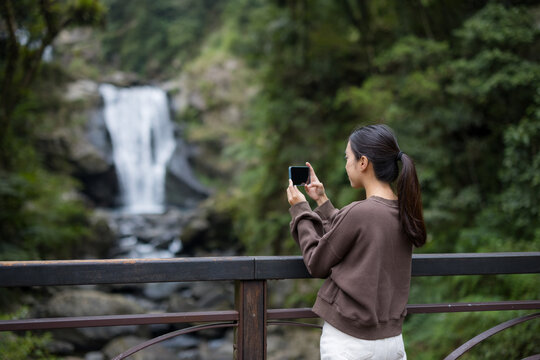 Woman use of mobile phone to take photo with waterfall in forest