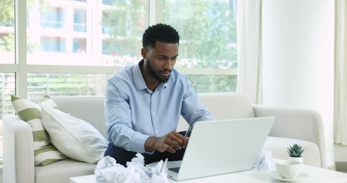 Angry African man hurrying finish paperwork, lost patience throwing crumpled papers feels stressed, having nervous breakdown due to hateful job, backlog of unfinished projects, problems and deadline