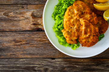 Crispy breaded seared chicken cutlet with lemon slices and fresh vegetables on wooden table

