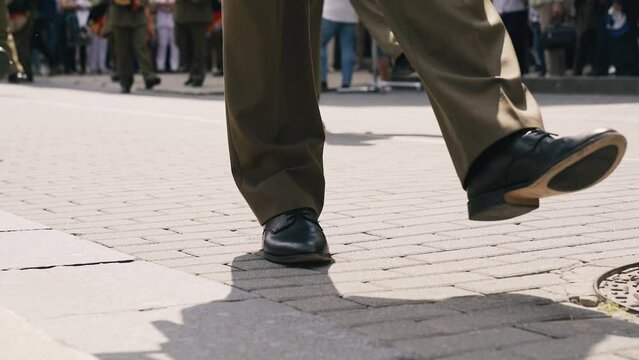 Military men are marching down the street. Close-up of legs.