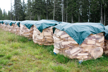 Stacks of firewood are covered with a tarpaulin to protect from the rain. Preparing for winter. Heating season