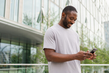 African american man holding smartphone touch screen typing scroll page on urban street in city. Guy with cell phone surfing internet using social media apps shopping online. Cellphone addiction