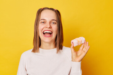 Laughing charming positive young girl with ponytails in jumper holding marshmallow posing isolated...