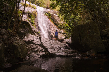 Young man in a Beautiful landscape of tropical waterfall and river inside lush green jungle in the Atlantic Rainforest, in Ilha Grande, Costa Verde, south Rio de Janeiro, Brazil