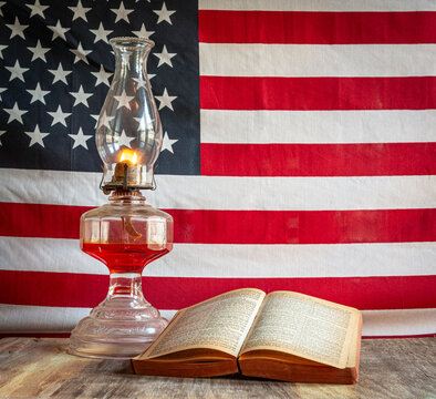 Open Holy Bible and old fashioned oil lamp with American flag background square