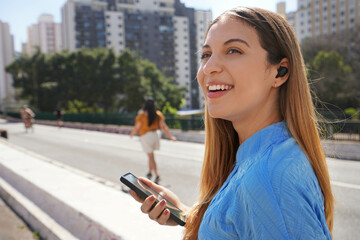 Fototapeta premium Close-up of smiling Brazilian girl listening music with her earbuds in Sao Paulo, Brazil