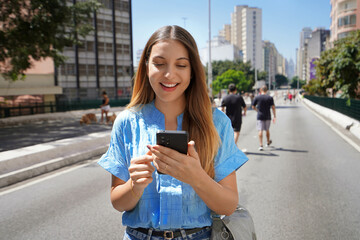 Portrait of cheerful Brazilian girl using mobile phone on Minhocao highway on sunday, Sao Paulo, Brazil
