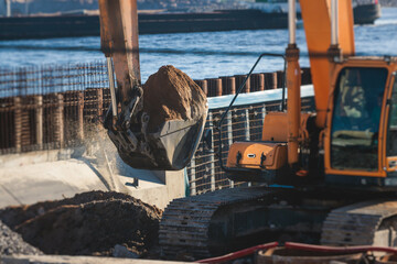 Excavator unloading sand into the dump truck on the construction site, excavating and working during road works, backhoe and tipper truck unload road metal and gravel, construction of the new road - obrazy, fototapety, plakaty