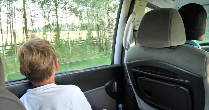The boy looks out the open car window. The family travels around the country in Manish on vacation. The family spends time traveling in their minivan during the summer. Family travel concept by car.