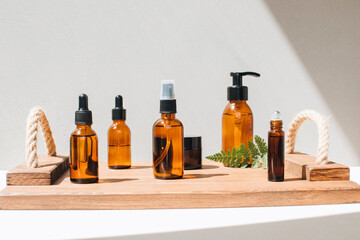 Amber bottles with facial cosmetics, liquid on a wooden tray on the light concrete background. Front view