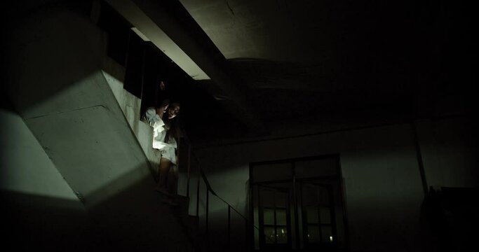 Horror scene of a mysterious Scary Asian ghost woman creepy have hair covering the face sitting on staircase at abandoned house with background dark scene movie at night, holiday ghost Halloween