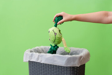 Woman putting a broken toy in waste bin on a green background