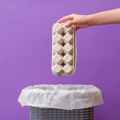 Woman putting an empty egg packing in waste bin on a violet background