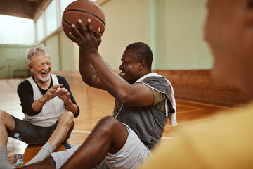 Diverse group of senior men taking a break from playing basketball in an indoor basketball gym