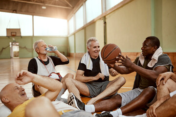 Diverse group of senior men taking a break from playing basketball in an indoor basketball gym