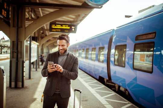 Young Caucasian businessman using a smartphone while waiting for his train at the train station