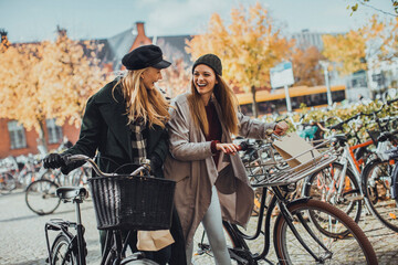 Young Caucasian female friends shopping together and pushing their bicycles through the city