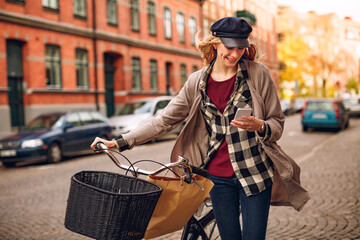 Young woman using a smartphone while pushing her bicycle in the city