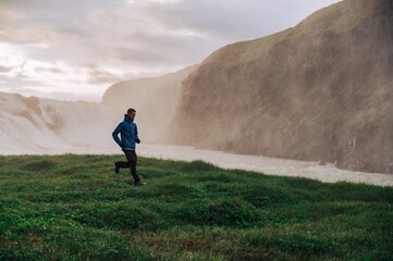 A sportsman is running in nature next to the waterfall in Iceland.