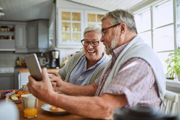 Senior Caucasian couple using a smartphone while having breakfast together in the kitchen in the morning