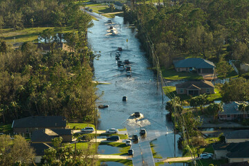 Hurricahe fainfall flooded Florida road with evacuating cars and surrounded with water houses in suburban residential area