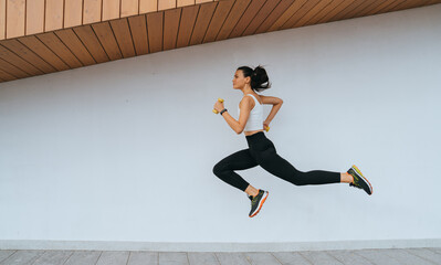 Strong young fit woman in sportswear running at public sport yard. Focused female runner preparing...