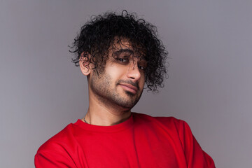 Fototapeta na wymiar Portrait of confident proud satisfied handsome bearded man with curly hair, looking at camera with smile, wearing red jumper. Indoor studio shot isolated on gray background.
