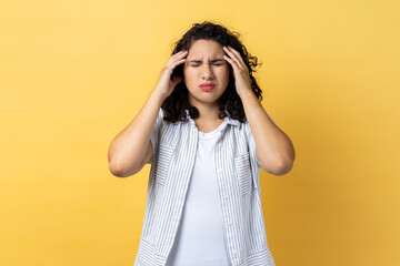 Portrait of woman with dark wavy hair frowning and clasping sore head, suffering intense headache,...