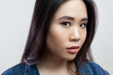 Closeup portrait of serious concentrated beautiful young adult brunette woman with makeup and long hair, looking at camera. Indoor studio shot isolated on gray background.