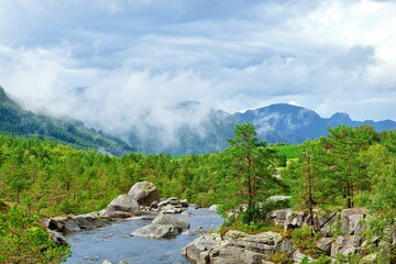 Fototapeta na wymiar Small stream flows through the rocky area surrounded by lush green mountain