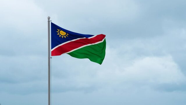 Namibia flag waving in the wind, cloudy blue sky with running clouds, endless seamless loop