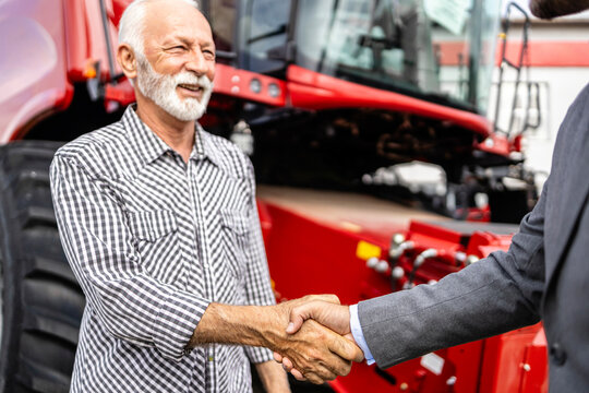 Investing in new agricultural machinery. Farmer and dealer shaking hands after tractor purchase.