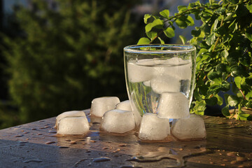 A glass of water with ice and ice cubes on a table top in the garden