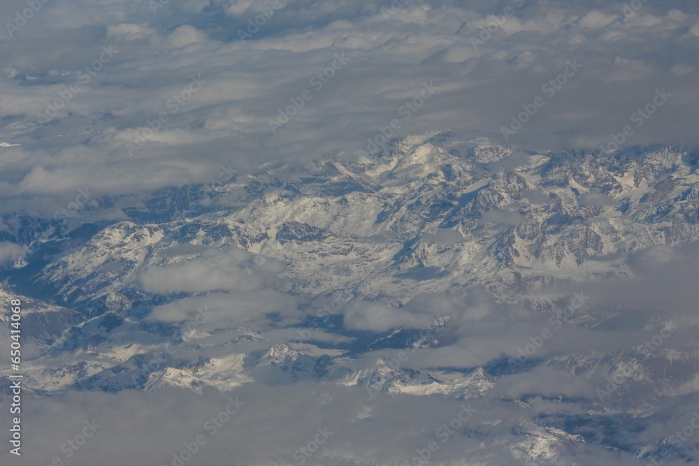 Poster aerial view of a mountain range covered with snow in clouds