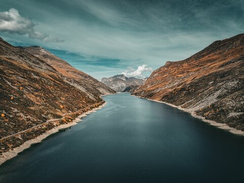 Aerial view of a tranquil lake surrounded by mountains on a cloudy day in Montespluga, Italy