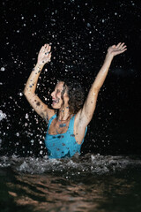 A beautiful and curly young woman in a blue swimsuit in the sea at night frolicking in the water