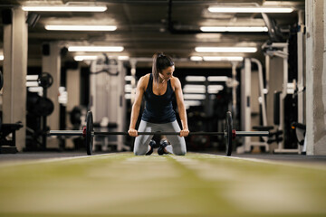 Fototapeta na wymiar A fit female bodybuilder is preparing to lift barbell in a gym.