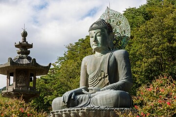 Large statue of Buddha seated atop a cement rock monument in front of a lush green mountain in Korea
