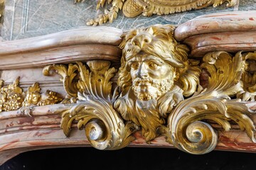 Close up of a gilded wood engraving of Hercules wearing a lion mane mounted to a marble fireplace