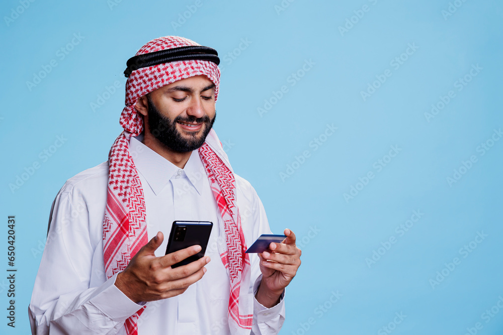 Aufkleber smiling muslim man using debit card to pay online while shopping in internet store with smartphone. 