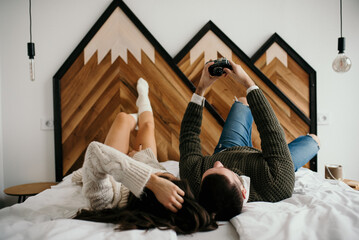 Young couple laying in bed, happily taking selfies with a camera smiling