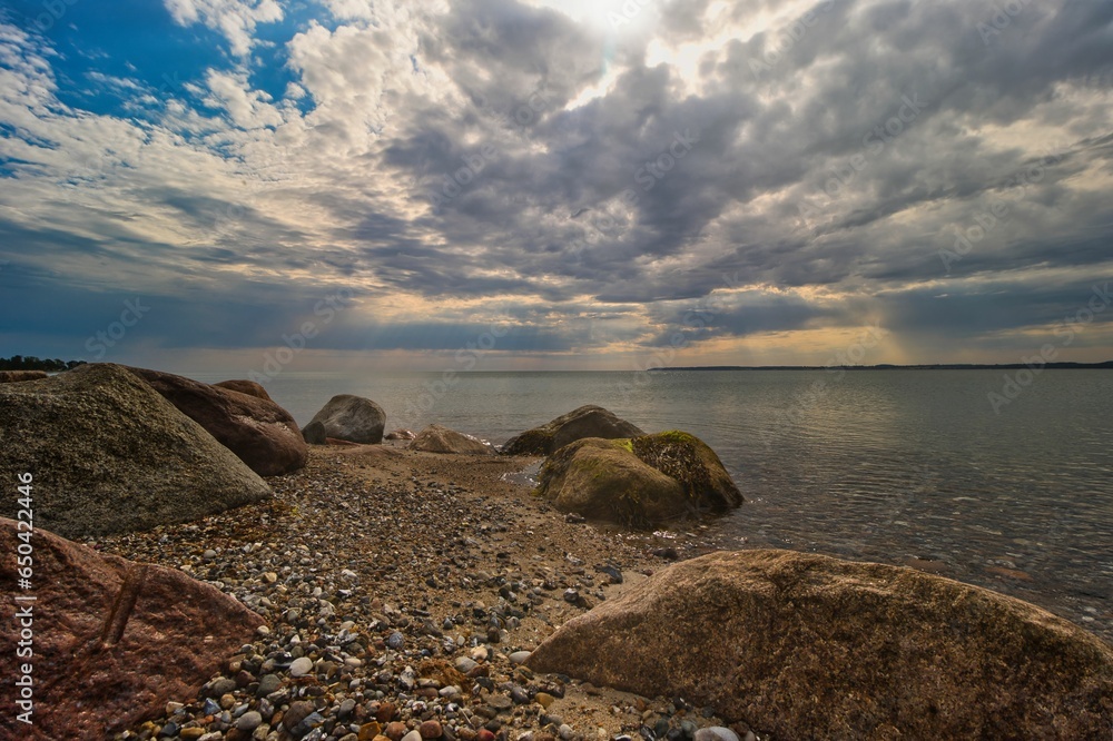 Wall mural sun breaks through clouds as it shines down on rocks in the middle
