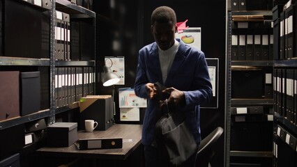 Exiting the evidence room, male private detective closes his personal computer. African American...