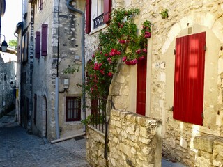 a narrow street with stone buildings and red shutters and flowers: Viviers, France