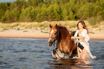 Beautiful woman and her horse galloping through the water on a beach
