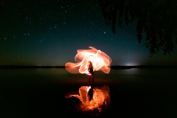 Long exposure shot of light trails being reflected on the lake under a starry sky