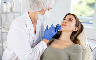 Young brunette woman having facial injection at bright treatment room with big window at background at aestetic center