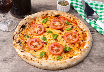 Margherita style pizza over wooden table with wine, oregano and spatula